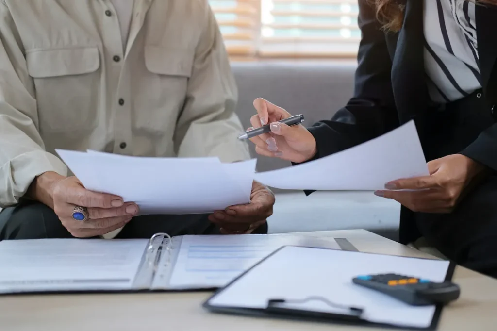 « Two people reviewing documents and a binder during a consultation »