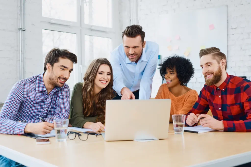 « Team of five colleagues gathered around a laptop in a bright office »